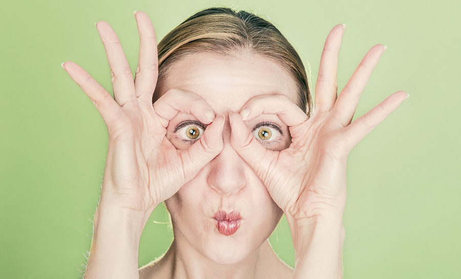 Fotografía en color de mujer mostrando sus ojos a traves de sus manos.